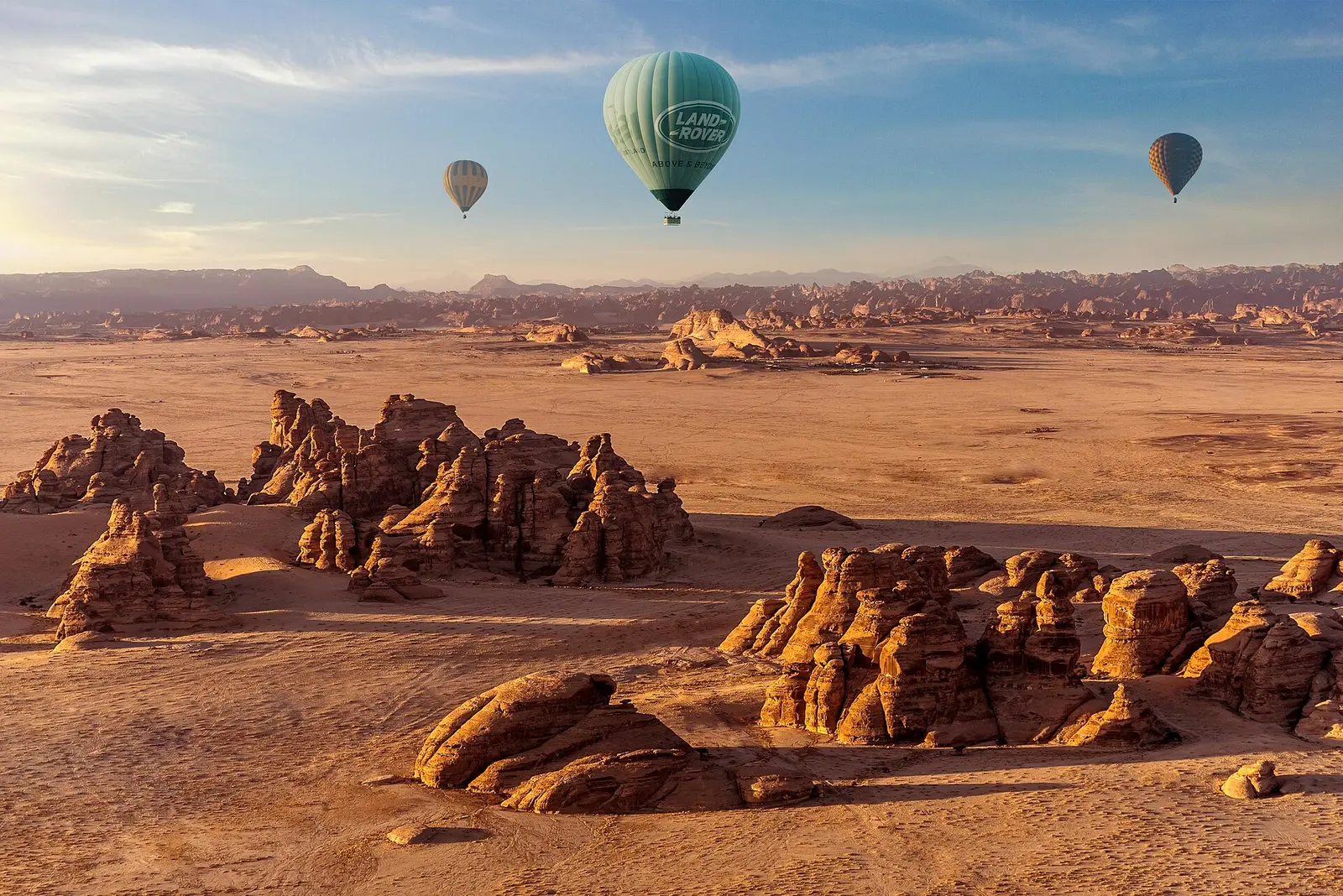 Hot air balloons flying over sandstone rock formations in AlUla